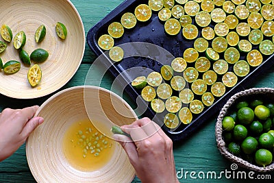 People hand squeeze juice out of kumquat fruits cut in half into bowl Stock Photo