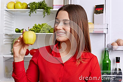 People and healthy nutrition concept. Adorable young woman with cheerful expression, holds green fresh apple, demonstrates her bre Stock Photo