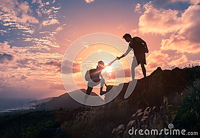 People helping each other hike up a mountain at sunrise. Giving a helping hand. Stock Photo