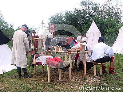 People knights in medieval costumes resting on the ground near the tents before the battle of the Vikings Editorial Stock Photo