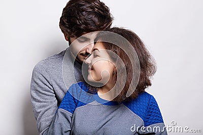 People, love and relations. A sylish couple standing over white background. Fashionable bearded man wearing grey sweater hugging h Stock Photo