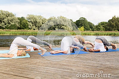 People making yoga in plow pose on mat outdoors Stock Photo