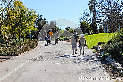 People in masks walking along a long paved walking path in the garden with lush green trees and plants along the path Editorial Stock Photo