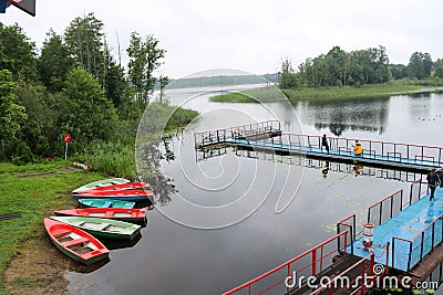 People, men are fishing from the pontoon, apron, bridge on the lake with ducks and boats on the shore at the recreation Editorial Stock Photo