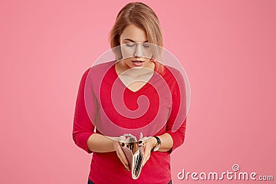 People and money concept. Shocked blonde European woman looks with surprisement at empty wallet, has to pay debts, dressed in red Stock Photo