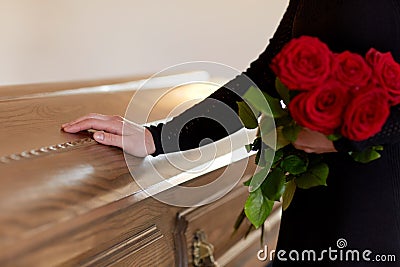 Woman with red roses and coffin at funeral Stock Photo