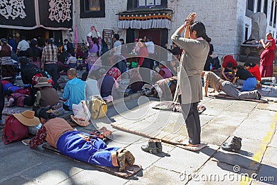 People praying in prostration in front of Jokhang temple in Lhasa on Barkhor square, Tibet - one woman standing Editorial Stock Photo
