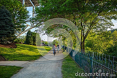 People riding bicycles on a path, under green trees. A place for relaxation and activities. Pittsburgh, Pennsylvania, USA Editorial Stock Photo
