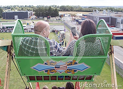 People in seats on ferris wheel fun fair carnival ride. Woman taking ariel photo on mobile phone Editorial Stock Photo