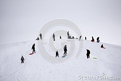 People in silhouette having fun on a snowy hilltop with adults and children sledging Stock Photo