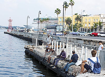 People sitting on cement wall fishing by the Malecon in Havana Cuba Editorial Stock Photo