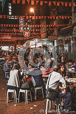 People sitting and eating street food at the evening Temple Street Market in Hong Kong Editorial Stock Photo