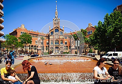 People are sitting near small fountain near Building of Old Hospital de Sant Paul in Barcelona, Spain Editorial Stock Photo