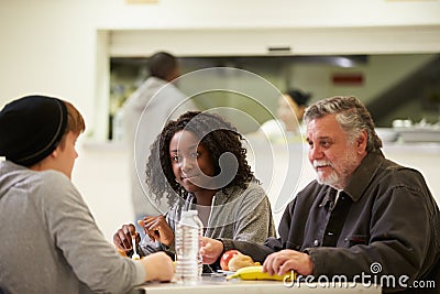 People Sitting At Table Eating Food In Homeless Shelter Stock Photo