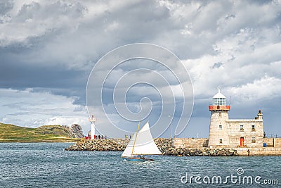 People on a small sailboat exiting Howth marina, passing Howth Lighthouse and per Stock Photo