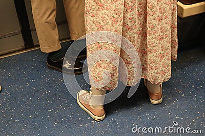 People stand in the train. look at their shoes. girl in a long pink dress and pink sneakers Stock Photo