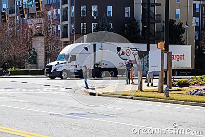 People standing on a corner at an intersection with a white semi truck turning the corner surrounded by apartment buildings Editorial Stock Photo