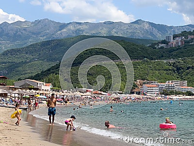 People sunbathe on the sandy beach and swim in the sea at the foot of the mountains Editorial Stock Photo