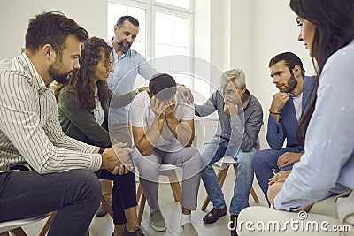 People supporting and comforting a crying young man during a group therapy session Stock Photo