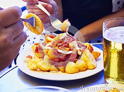 People taste a portion of Patatas Bravas over a metallic table. Fried potatoes topped with spicy sauce, also know as Patatas a la Stock Photo