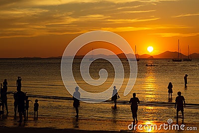 People, tourists enjoy a gorgeous sunset on a tropical beach. Silhouettes of people are all watching the sun. Golden tones. The Stock Photo