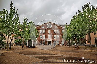 People on tree-lined path and brick building on cloudy day in Amsterdam. Editorial Stock Photo