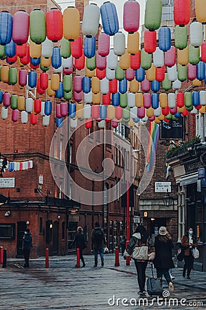 People walk under rainbow coloured lanterns on a street in Chinatown, London, UK Editorial Stock Photo