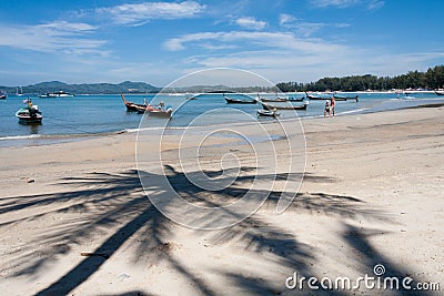 People walking on the beach, past boats with palm tree shadow, Bang Tao beach, Phuket, Thailand Editorial Stock Photo