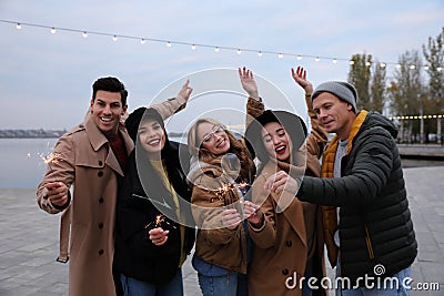People in warm clothes holding burning sparklers on pier Stock Photo
