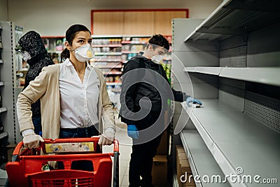 People wearing masks and gloves buying groceries/supplies in supermarket with sold out products.Food supplies shortage.Empty Stock Photo