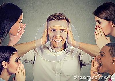 People whispering a secret gossip to a man who covers ears ignoring them Stock Photo