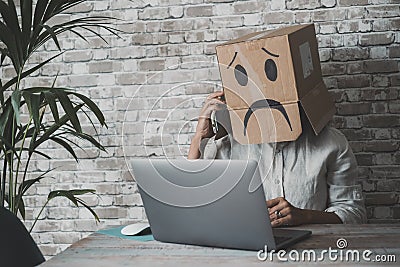 People at work with sad carton box on head diong phone call in front of a laptop on the desk. Sad worker anonymous. Business fail Stock Photo