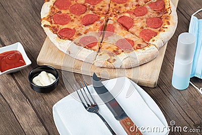 Pepperoni pizza on a wooden board with sauces, plate, hand sanitizer Stock Photo