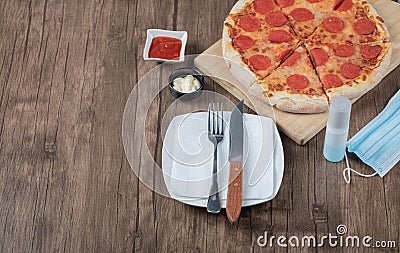 Pepperoni pizza on a wooden board with sauces, plate, hand sanitizer Stock Photo