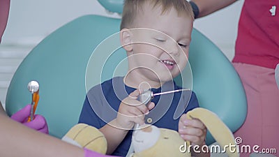 Pequeño muchacho despreocupado que se sienta en la silla en oficina dental Niño lindo que juega con el juguete de la felpa Tratam almacen de metraje de vídeo Pequeño muchacho despreocupado que se sienta en la silla en oficina dental Niño lindo que juega con el juguete de la felpa Tratam almacen de metraje de vídeo