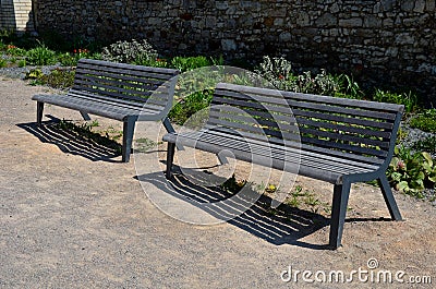 Perennial bed mulched with gray gravel in front of a limestone stone wall in a square with benches with wood paneling, beige path Stock Photo