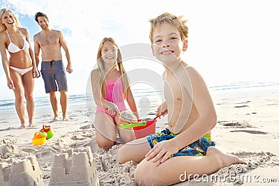 The perfect family getaway. a young brother and sister building a sandcastle on the beach while their parents stand in Stock Photo