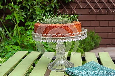 A perfect home baked sponge cake decorated with rosemary herb on crystal stand on green garden table Stock Photo