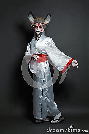 Perfect young woman wearing animal mask and white kimono standing on black background, full length portrait. Halloween, Carnival Stock Photo