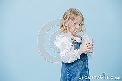 Perky little girl in jeans overalls sipping milkshake through a straw over blue Stock Photo