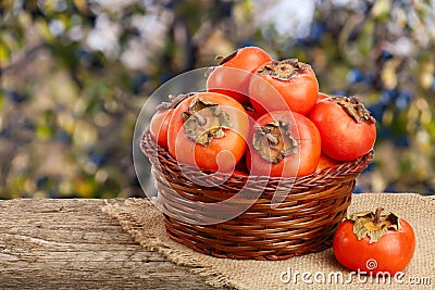 Persimmon fruit in a wicker basket on a wooden table with blurred garden background Stock Photo