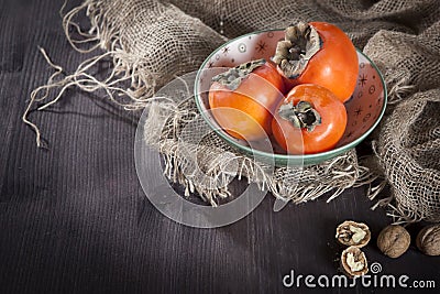 The persimmon in a plate on a napkin made of canvas on a dark wooden table Stock Photo