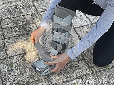 Bending person adjusting the velcro straps of the orthopedic walking boot, ideal for people with leg injuries such as tibia or Stock Photo