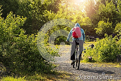 Person in blue hoodie and red backpack riding a bike in a country side. Cross country cycling concept. Adventure and outdoor Stock Photo