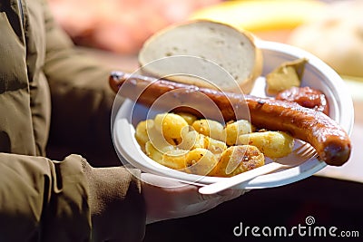 Person buy portion fried potatoes and sausages in disposable plate on famous open air Christmas fair in Krakow. Street food on Stock Photo
