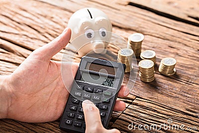 Person Calculating On Calculator With Coins And Piggy Bank Stock Photo