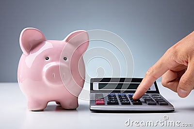 Person Calculating With Calculator Near Piggy Bank At Desk Stock Photo