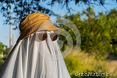 Person covered by a white sheet, with sunglasses and hat, in appearance of a ghost, in garden Stock Photo