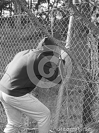 Person crawling through a fence opening with hand clinging to a steel wire , black and white Stock Photo