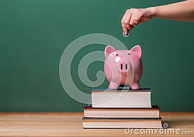 Person depositing money in a piggy bank on top of books with chalkboard Stock Photo